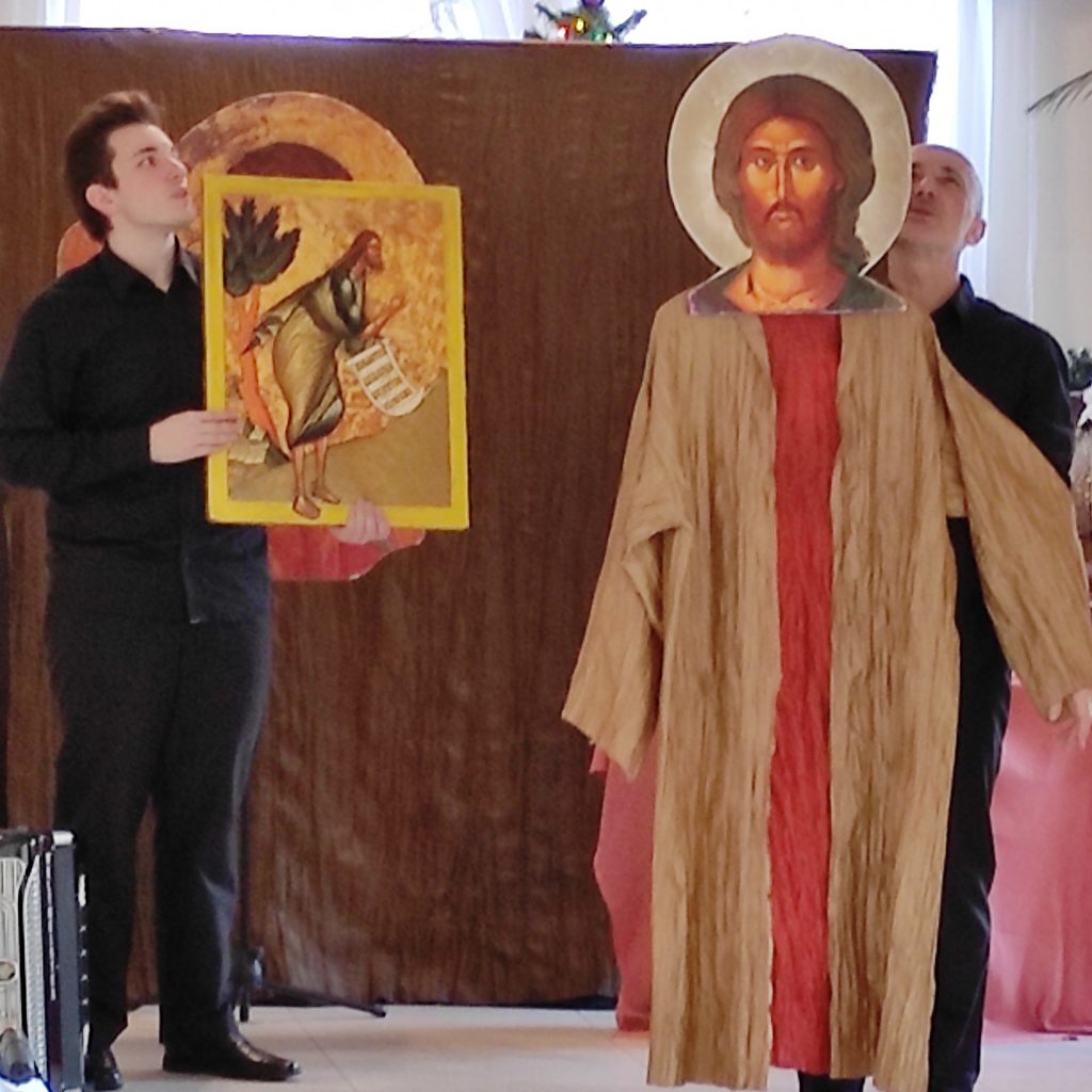 Aktorzy recytujący słowa z ewangelii św. Łukasza. Jeden z nich trzyma w ręku ikonę przedstawiającą postać Jana Chrzciciela a drugi trzyma postać Pana Jezusa.