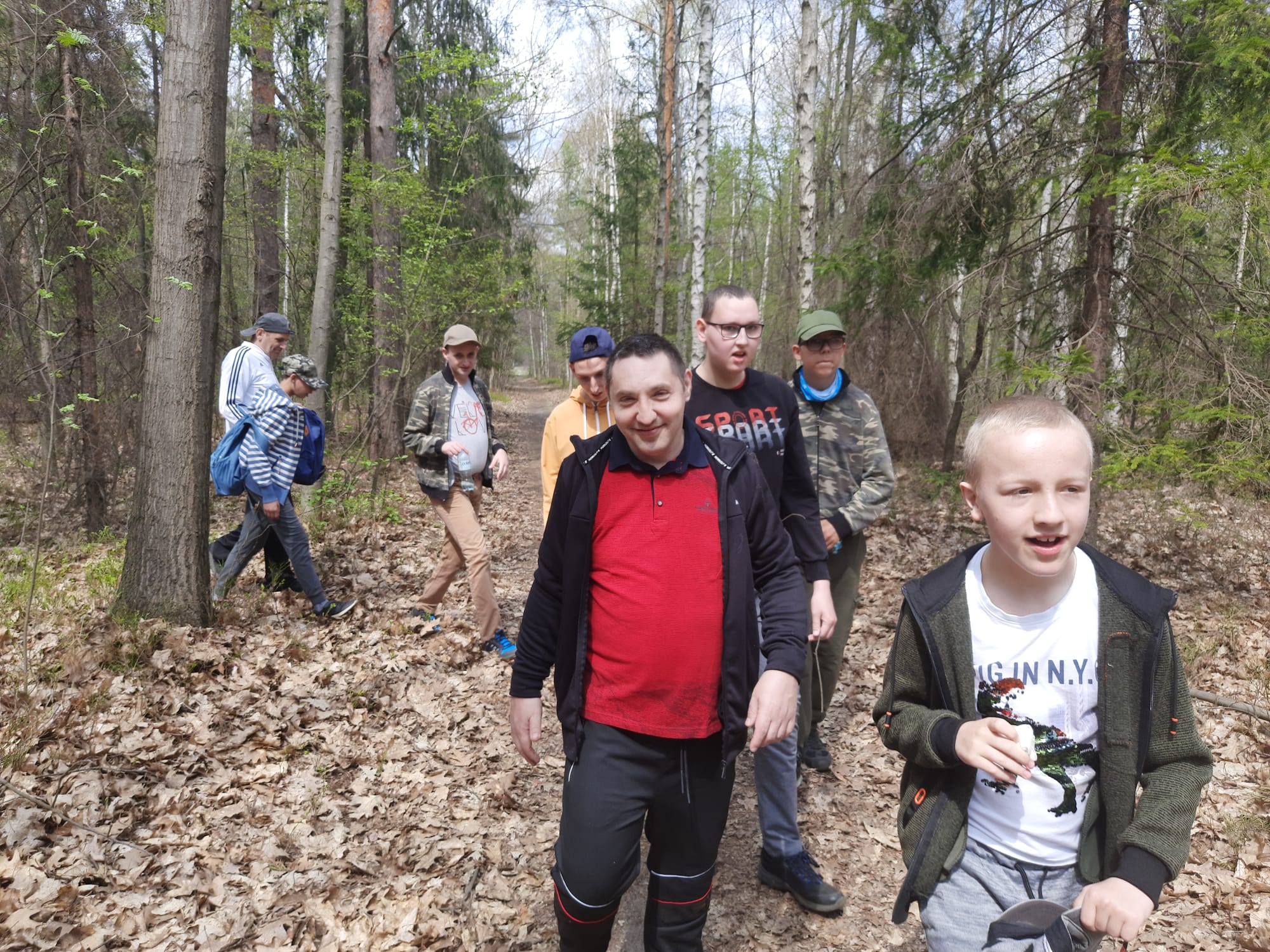Zdjęcie grupowe przedstawiające ośmiu mieszkańców  spacerujących w lesie.