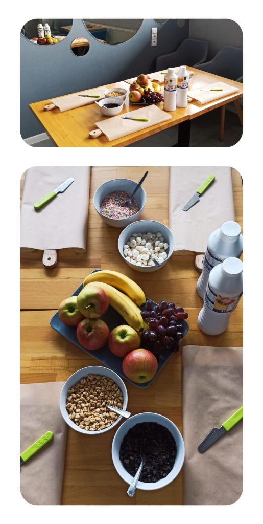 Kolaż z dwóch zdjęć. Jest na nich nakryty stół. Na stole są deski pokryte specjalnym papierem, noże oraz dodatki do gofrów: owoce (jabłka, banany, winogrona), polewy oraz różne rodzaje słodkich posypek.